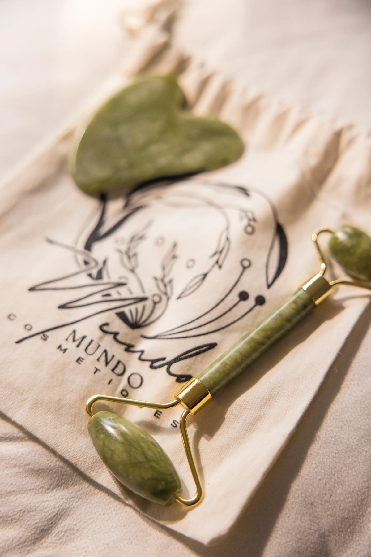 Image d'un rouleau de jade avec une pierre de gua sha posée et rangée sur un pochon en coton